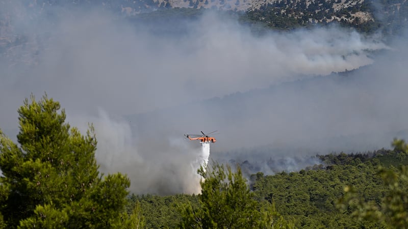 A firefighting helicopter drops water over a smoke-filled forest during a wildfire near Porto...